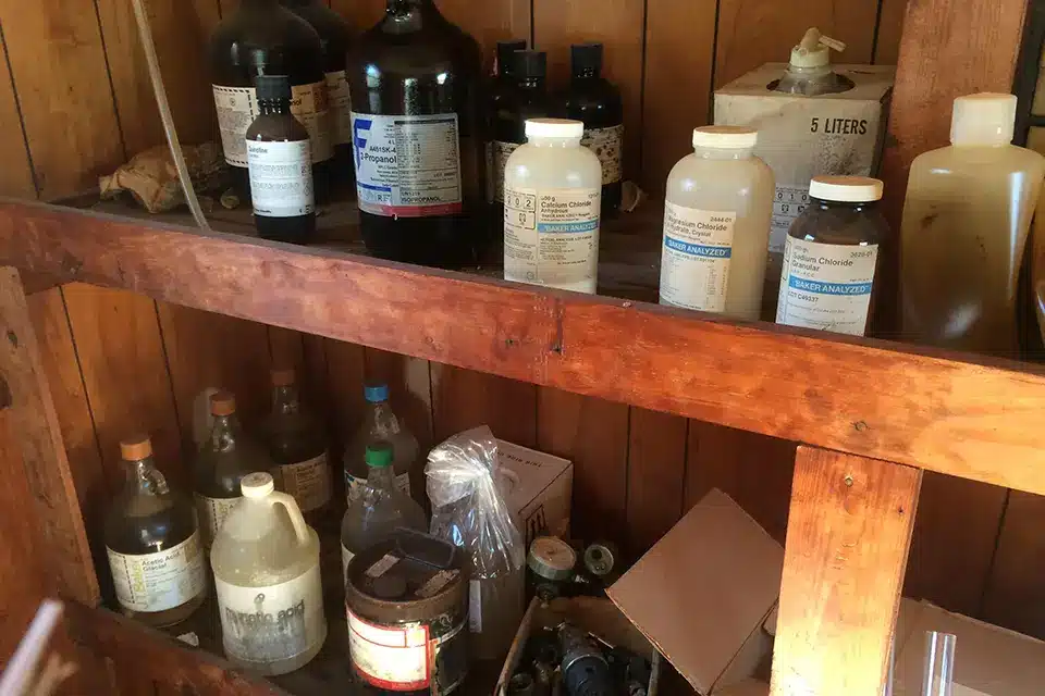 Shelf of old laboratory chemicals awaiting lab pack service.