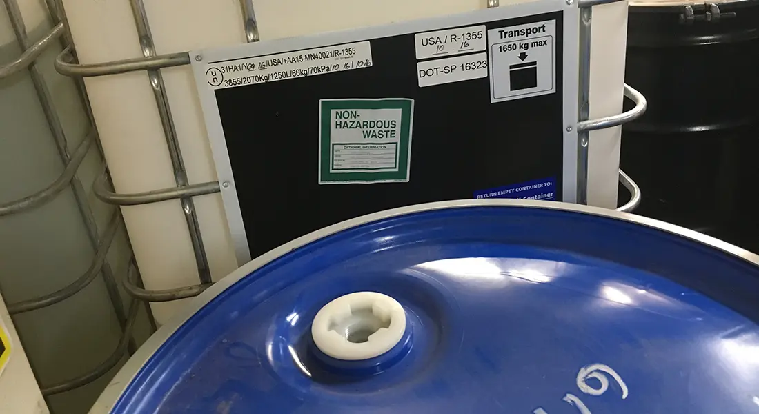 A DOT shipping label and waste identification on a tote staged for pickup.